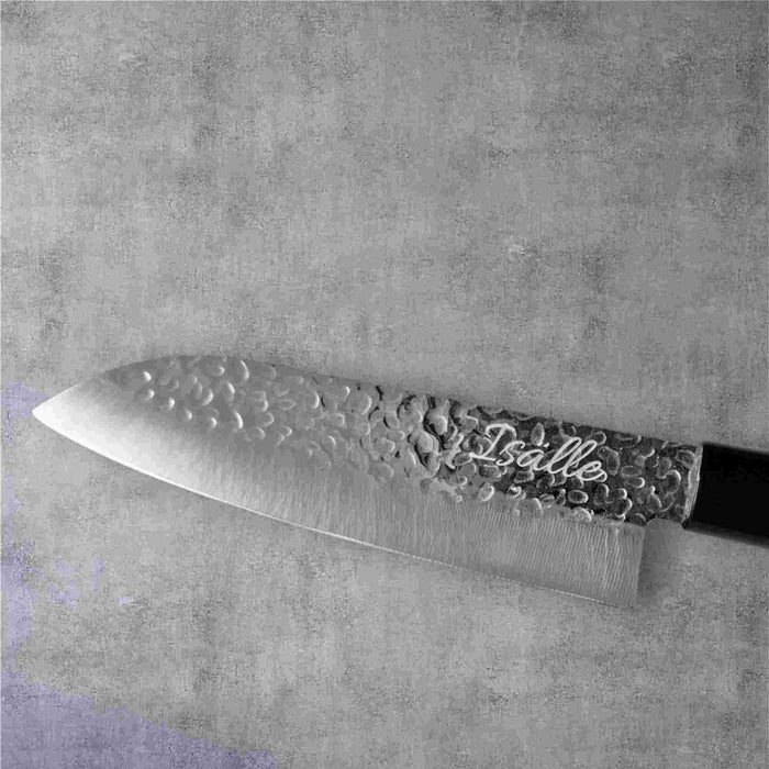 Japanilainen Santoku-veitsi, jossa on vasaroitu terä ja kaiverrettuIsalle"-teksti, harmaalla kivimäisellä taustalla.
